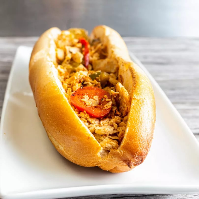 A close-up of a hot dog bun filled with shredded chicken, crispy onions, and a tomato slice.