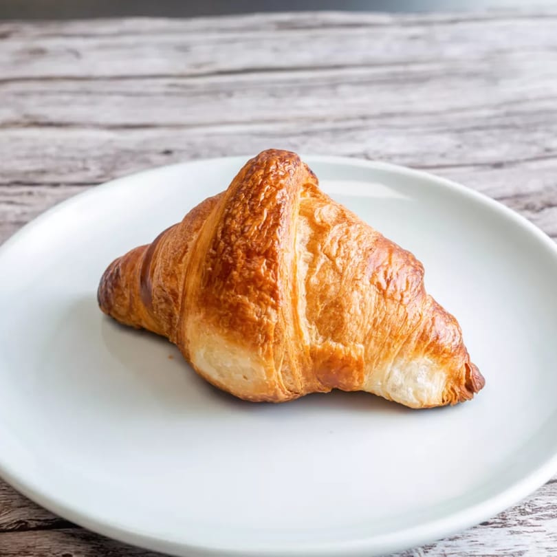 Golden-brown croissant on a white plate, with a rustic wooden background.