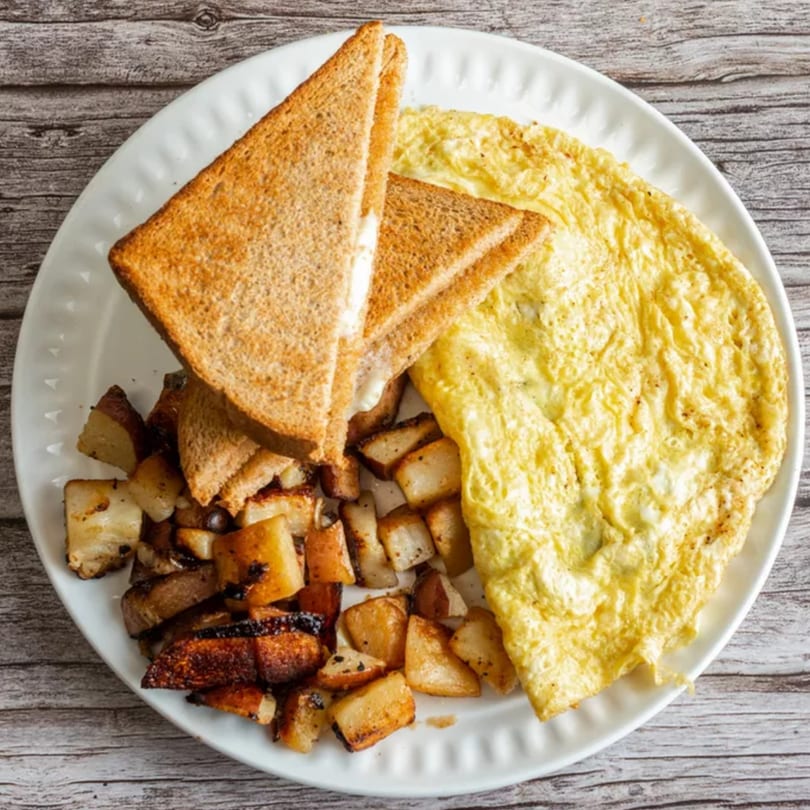 A breakfast plate with a fluffy omelet, golden-brown toast, and crispy home fries.