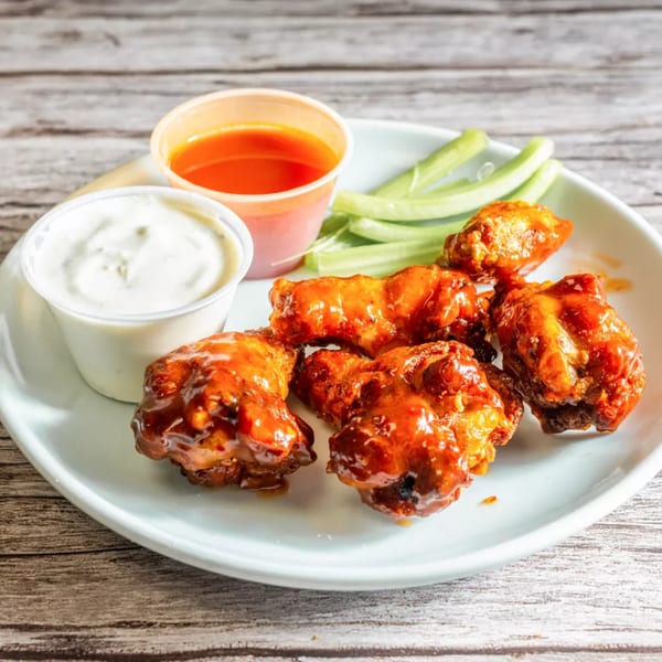 A plate of buffalo wings with celery sticks, ranch dressing, and hot sauce on a wooden table.